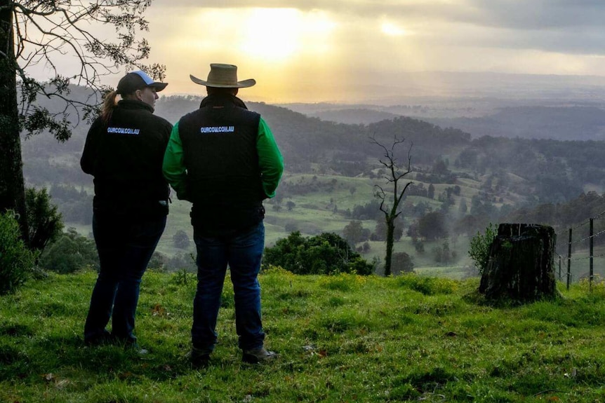 Image of two farmers standing at the top of a hill looking out at rolling green hills and pastures.