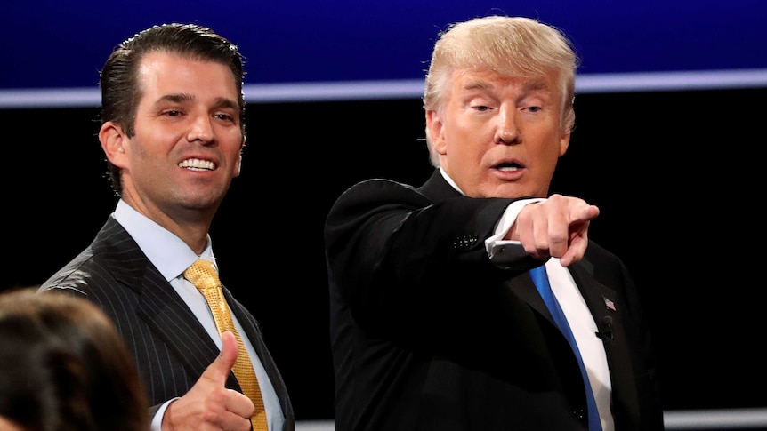 Donald Trump Jr smiles and gives a thumbs up while Donald Trump appears to point into the crowd.