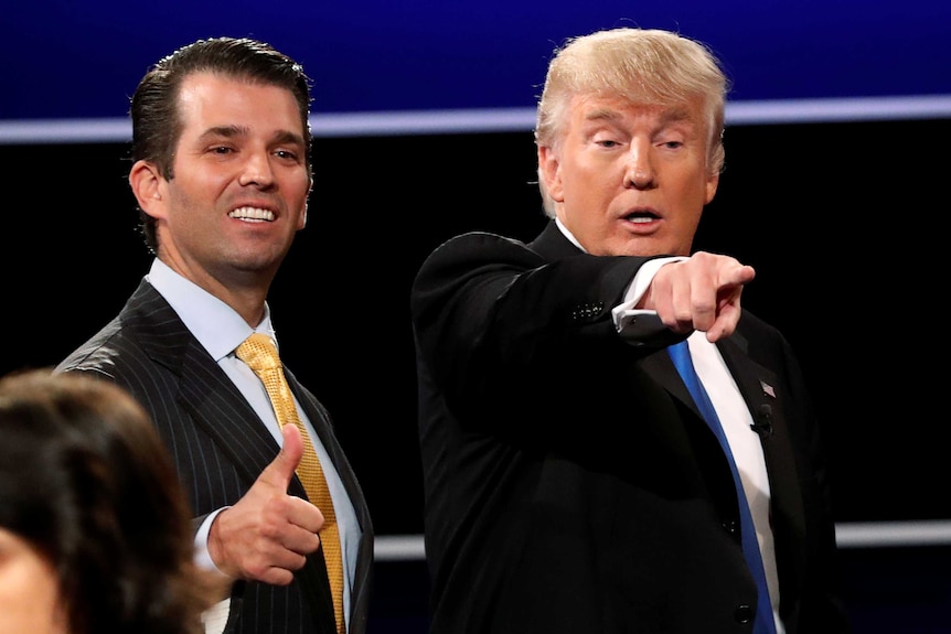 Donald Trump Jr smiles and gives a thumbs up while Donald Trump appears to point into the crowd.