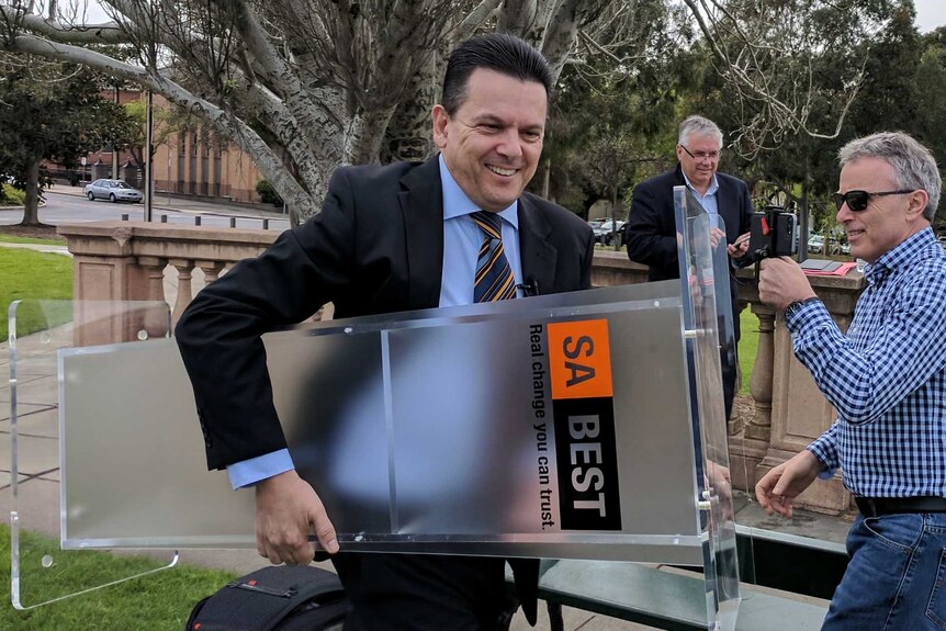 Nick Xenophon carrying a podium with an SA Best sign