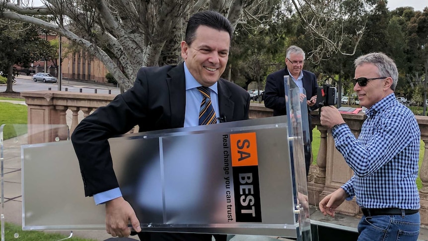 Nick Xenophon carrying a podium with an SA Best sign