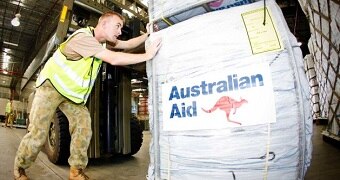 A person in army fatigues pushes a container with the Australian Aid logo on it.