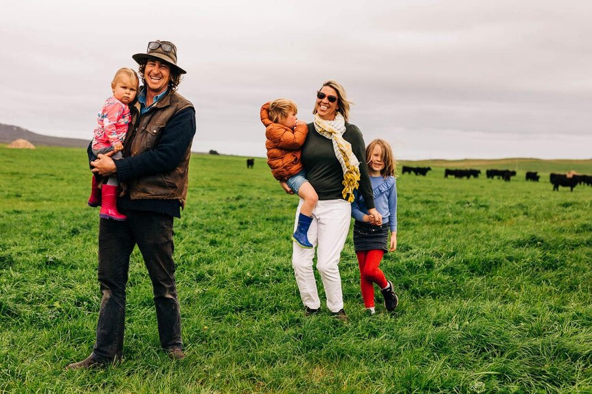 Flinders Island tourism operators Jo and Tom Youl smile as they lead their kids across a paddock.