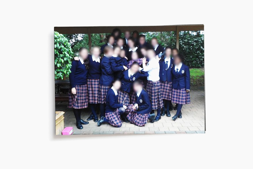A group around 20 young women in school uniform pose for a photo outdoors.