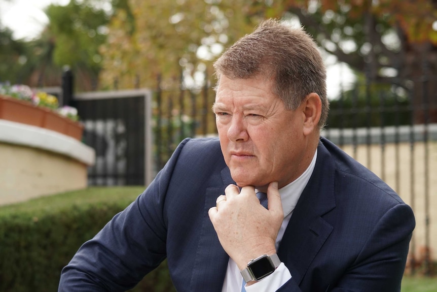 Man in suit sits at table with hand on chin