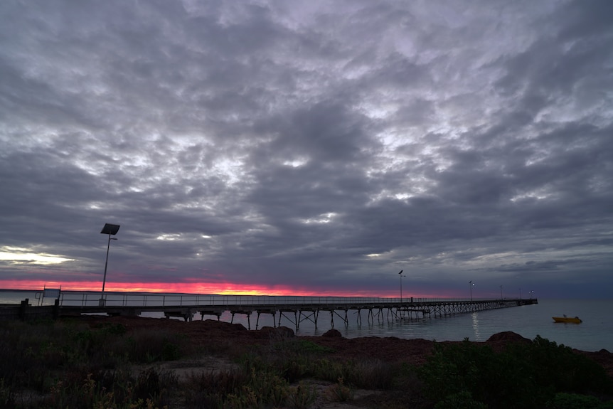 Looking over rocks towards a jetty at sunrise.