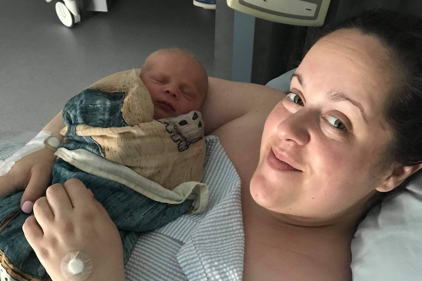 Emma Helks lying on a hospital bed holding new-born baby, Theo.