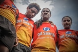 Low angle of four women from PNG dressed in rugby league uniforms standing.