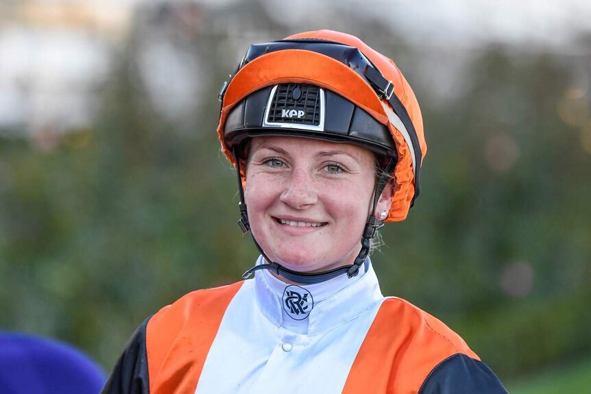 Jamie Kah smiles, in jockey outfit as she rides a horse at Flemington Racecourse.
