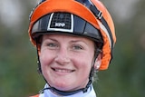 Jamie Kah smiles, in jockey outfit as she rides a horse at Flemington Racecourse.