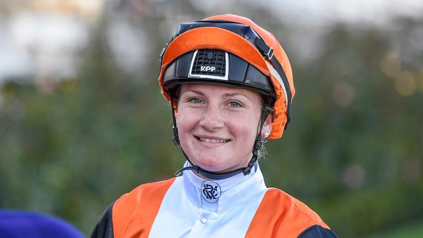 Jamie Kah smiles, in jockey outfit as she rides a horse at Flemington Racecourse.