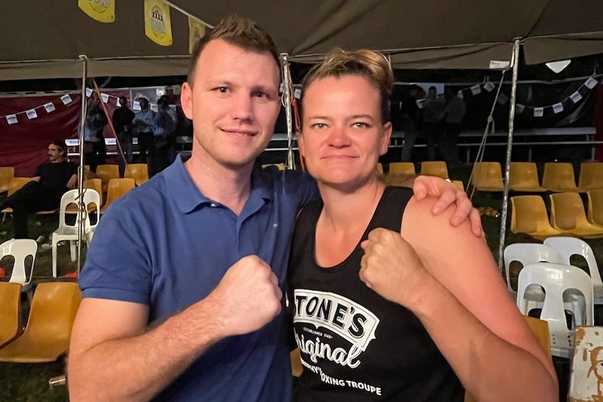 A male and female stand one arm around each other, the other in the typical fist stance used by boxers in pre-fight photos.