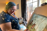 A woman wearing glasses paints a picture of horseriders
