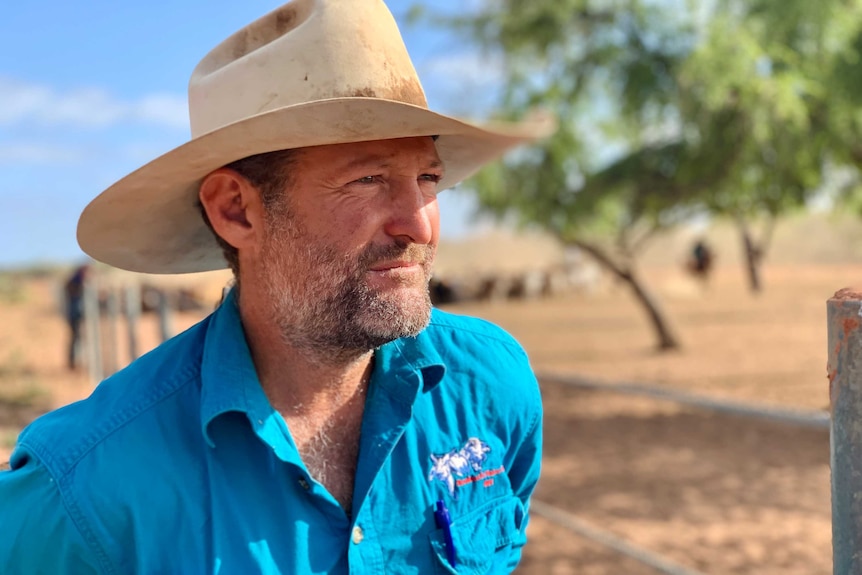 Portrait image of a man in a blue shirt wearing an akubra, staring out of frame.