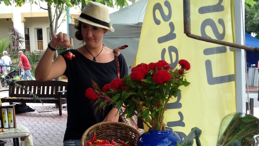 A lady takes a chilli from a basket of chillies at the produce stall and holds it up.