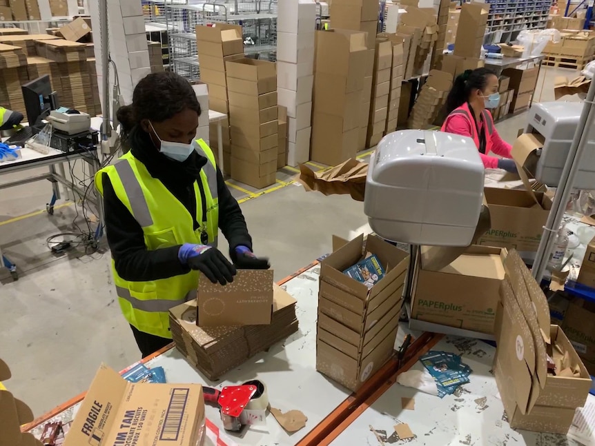 Two women pack cardboard boxes in a warehouse.