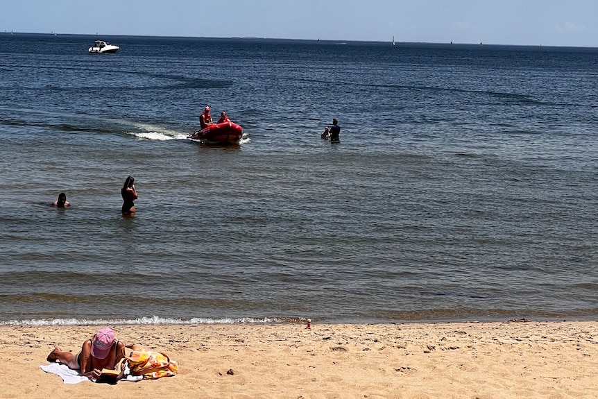 A lifeguard boat out on the surf as beachgoers wade through the water and sunbake on a hot day
