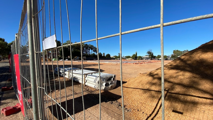 A photo taken through a fence at a construction site. There are pipes in the foreground..