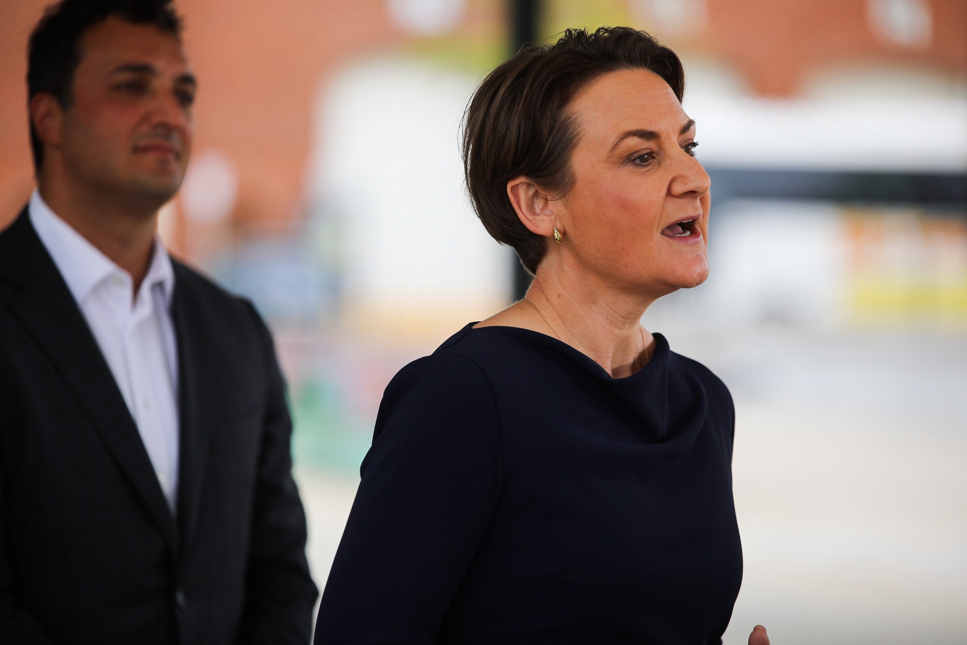 A woman with short, dark hair wears a dark outfit as she speaks.