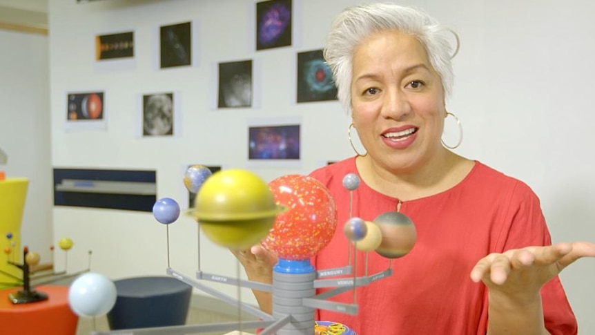 Female teacher in classroom with scale model of sun and planets in solar system
