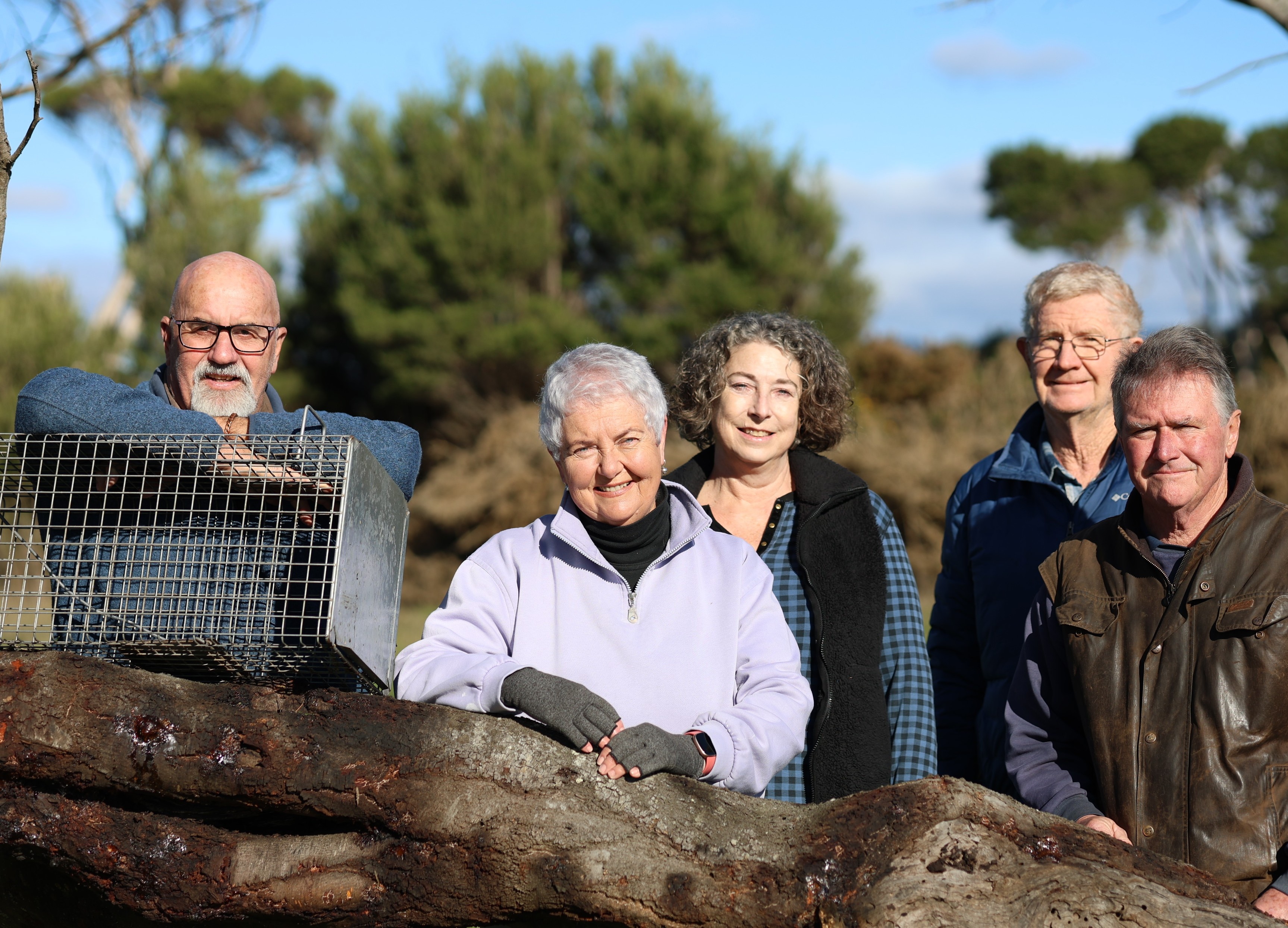 A man leans on a metal animal trap perched on a tree branch next to two women and two men