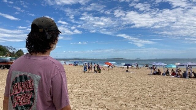 A young person with their back to the camera looking at Noosa beach on a sunny summer day