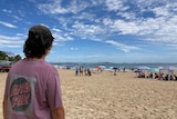 A young person with their back to the camera looking at Noosa beach on a sunny summer day