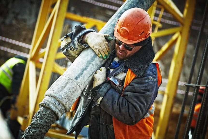 A construction worker pours cement or concrete using a pipe.
