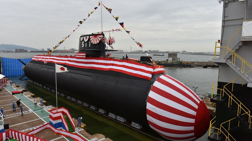 A large submarine, sitting out of the water, is decorated with fabric with colours from the Japanese flag