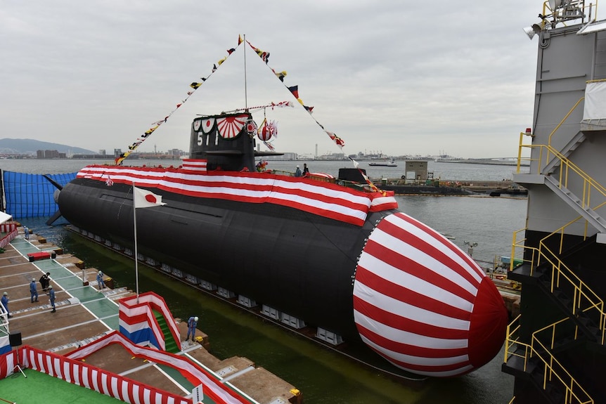 A large submarine, sitting out of the water, is decorated with fabric with colours from the Japanese flag