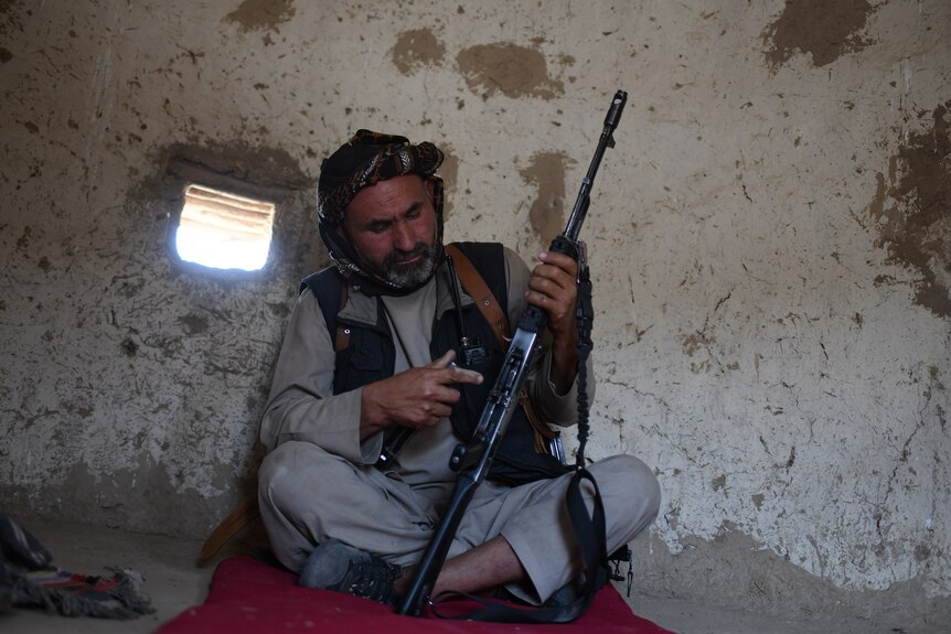 Man sits with folded legs, loading his rifle. 