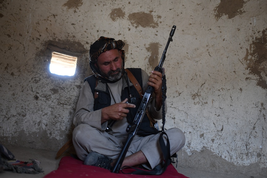 Man sits with folded legs, loading his rifle. 