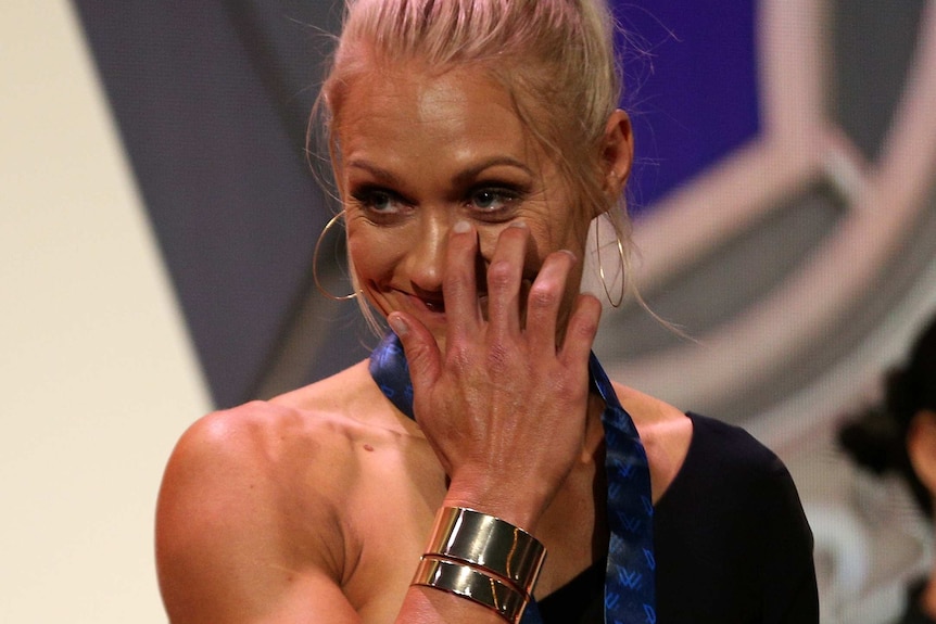 Erin Phillips wipes underneath her eye while smiling, with the AFLW medal around her neck.