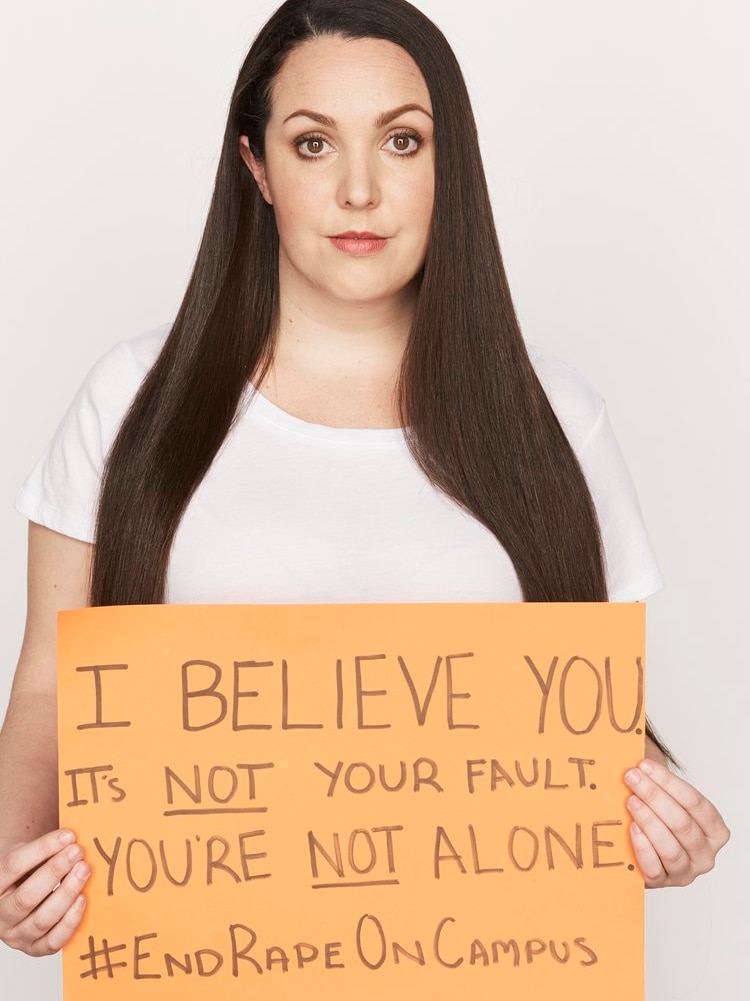 Nina Funnell holds orange placard saying: I BELIEVE YOU. It's not your fault. You're not alone. #EndRapeOnCampus