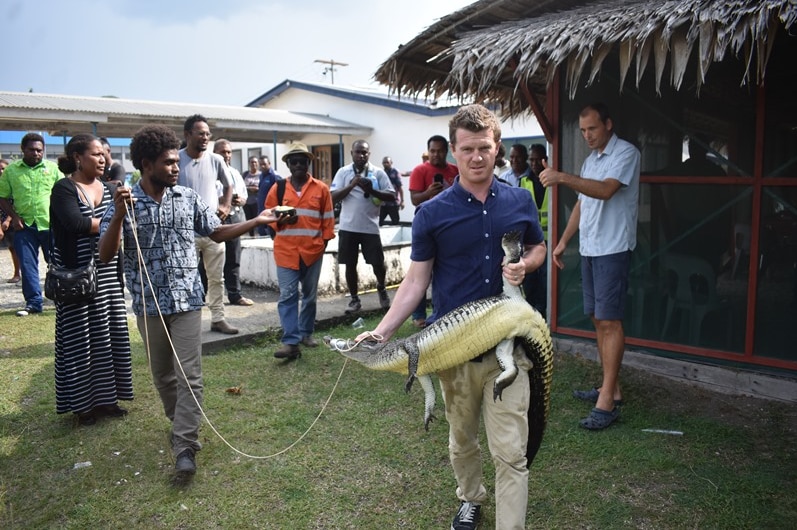 Matthew Brien holds a small crocodile by the mouth and back leg.