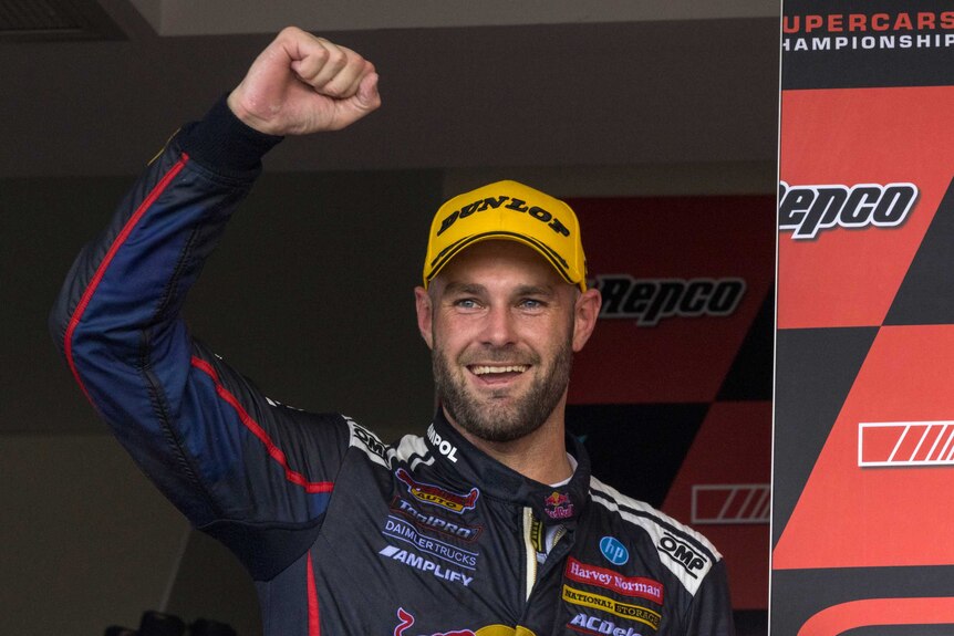Race driver with a fist in the air celebrates winning a race.