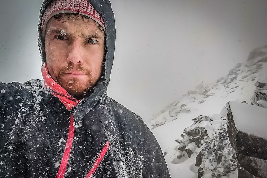 Man in a spray jacket on a mountain covered in snow.