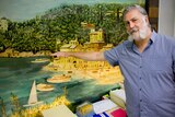 Man has arm out near shoulder height to demonstrate level of 1974 flood in Lismore on a wall mural