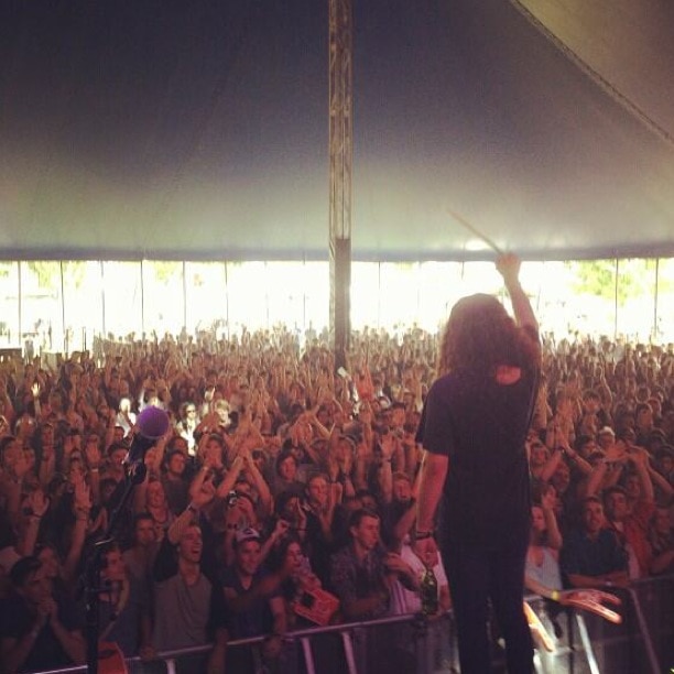 A mann holds a drumstick up to a big crowd inside a tent at a festival