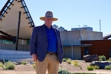 A white man in a blue shirt, jacket and hat standing in front of the line of lode Broken Earth Complex in Broken Hill