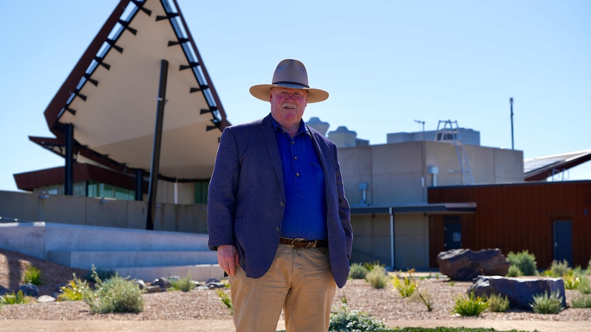 A white man in a blue shirt, jacket and hat standing in front of the line of lode Broken Earth Complex in Broken Hill