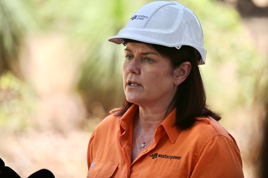 A woman wearing an orange shirt and a hard hat speaks.