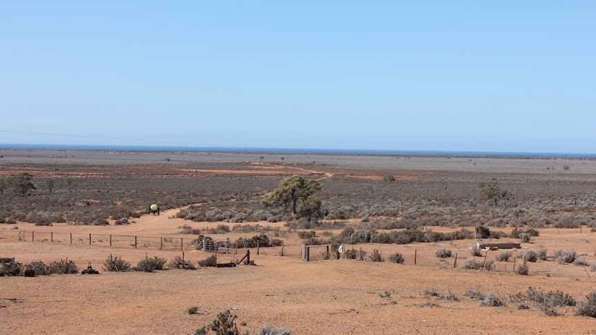 A vast dry station covered in shrubs with the shoreline in the background.