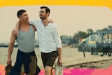 Two men in Bros are seen strolling along a beach happily, with their arms around each other. One is muscly, the other thin.