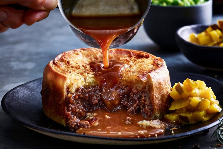 a picture of gravy being poured onto a flaky meat pie made out of goat