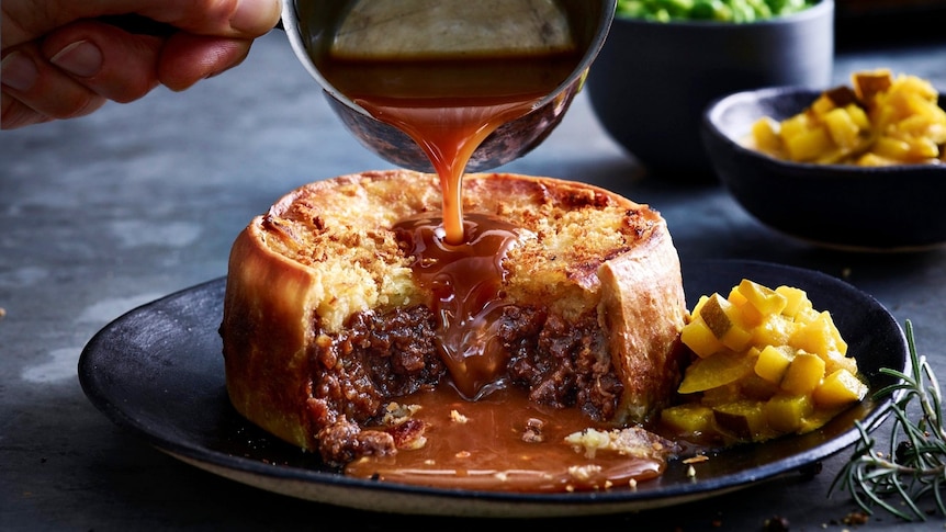 a picture of gravy being poured onto a flaky meat pie made out of goat
