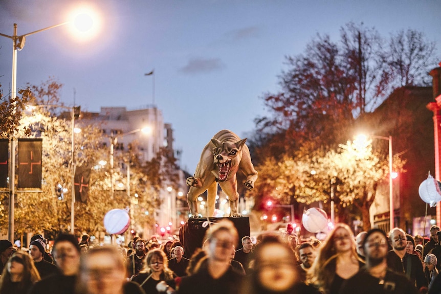 A crowd of people at night leading a sculpture of an animal