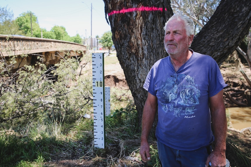 A man next to a pink line flood marker on a tree.