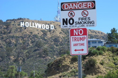 A street sign that says 'No Trump Anytime', an art installation by Plastic Jesus, is seen below the iconic Hollywood sign.