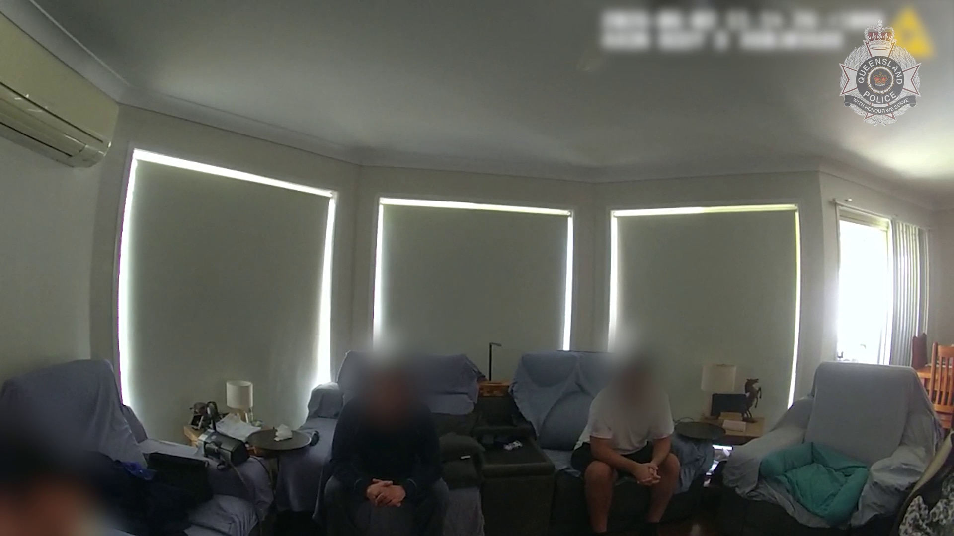 Two people with faces blurred sit on a couch indoors